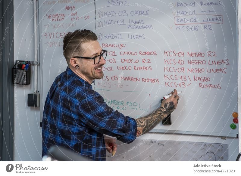 Fröhlicher Mann, der in einer Werkstatt auf ein Whiteboard schreibt schreiben zur Kenntnis nehmen Kunstgewerbler Markierung heiter Meister Kunsthandwerker