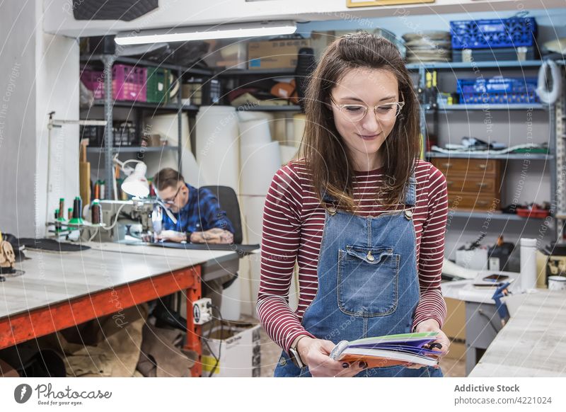 Lächelnde Handwerkerin mit Notizbuch in der Werkstatt Notebook Notizblock Atelier Kunstgewerbler Planer kreativ Arbeit Frau Handwerkskunst Kunsthandwerker