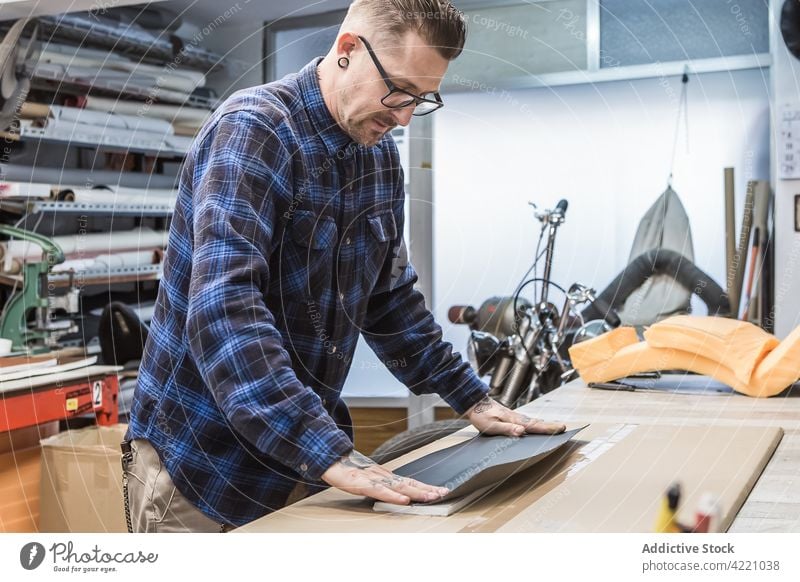 Bärtiger Handwerker, der an der Werkbank Motorradsitze polstert Kunsthandwerker Werkstatt Gewebe Stoff Polsterung Kunstgewerbler Hipster kreieren Hobelbank