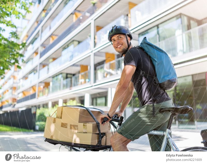 Fahrradkurier, der eine Lieferung auf einem Lastenfahrrad macht Menschen junger Erwachsener Mann männlich Lächeln Glück blauer Kragen Kurier Meldereiter