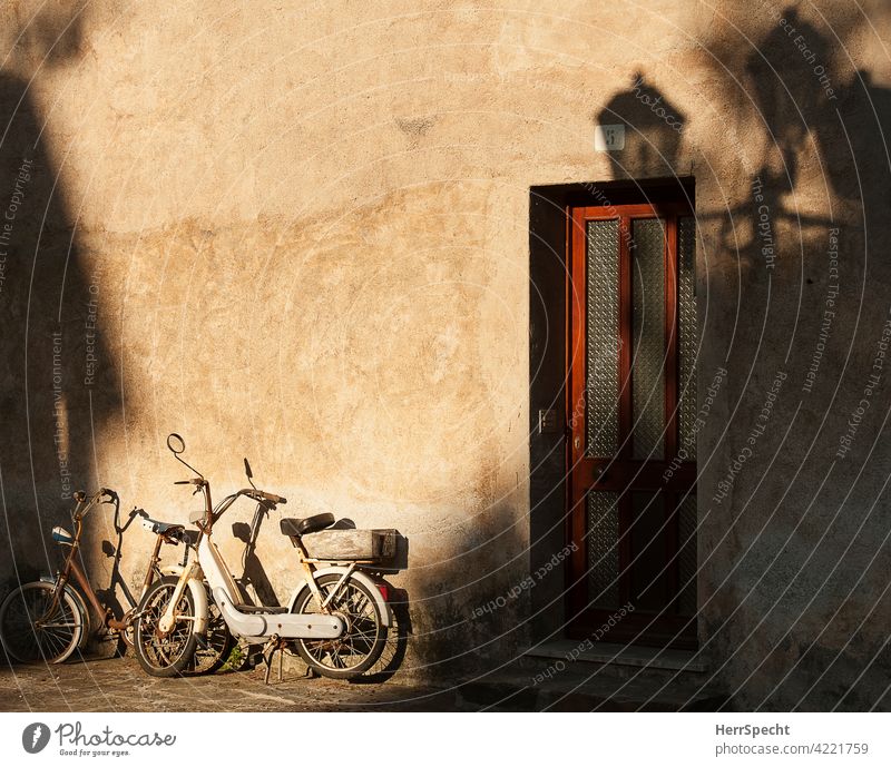 Rad und Mofa an Hauswand in der Morgensonne in Italien Fahrrad moped Schattenspiel Außenaufnahme Motorrad Gebäude parken Haustür Laternenschatten Italienisch