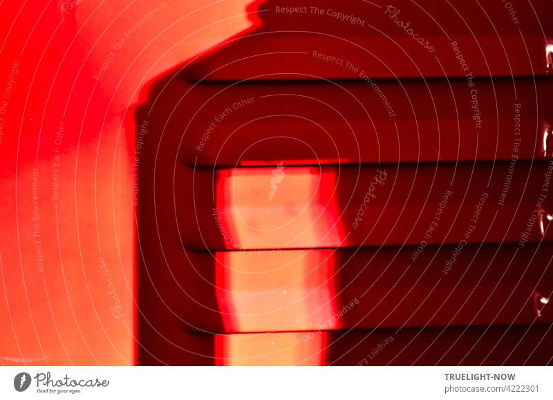 Rot! Sonnenlicht und Schatten auf der Tür (Detail) eines Feuer roten Metallschranks mit Lüftungsschlitzen die an der Seite noch kleine weisse Lichtreflexe zeigen