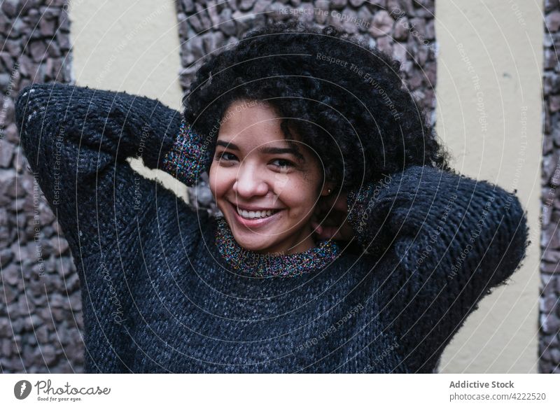 Glückliche ethnische Frau mit lockigem Haar in der Stadt Afro-Look Frisur Lächeln charmant krause Haare Vorschein Haare berühren Schönheit natürlich heiter