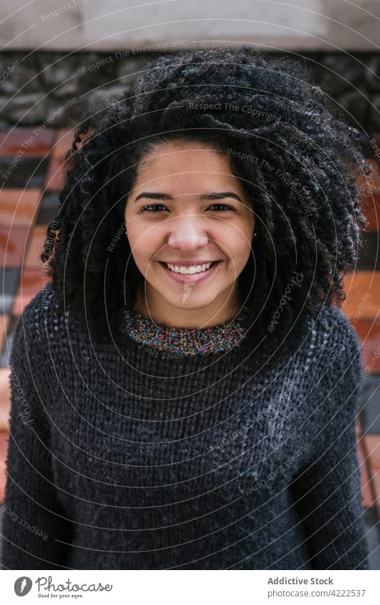 Glückliche ethnische Frau mit lockigem Haar Afro-Look Frisur Lächeln charmant krause Haare Vorschein Schönheit natürlich heiter Großstadt jung froh Straße