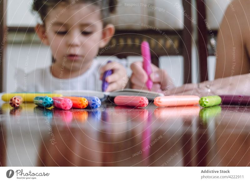 Crop Mutter und Kind zeichnen zusammen zu Hause Zusammensein Kinderbetreuung Markierung Filzstift heimwärts kreativ Bildung Notebook Tisch wenig Kindheit Hobby