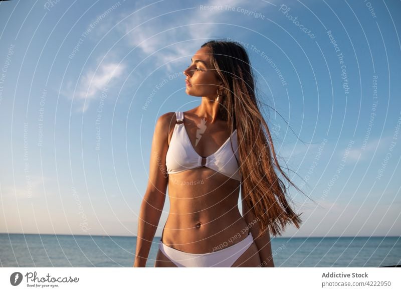 Modell im Badeanzug am Strand gegen das Meer MEER Körper Badebekleidung feminin selbstbewusst Meereslandschaft Frau Porträt Blauer Himmel sandig Natur wolkig