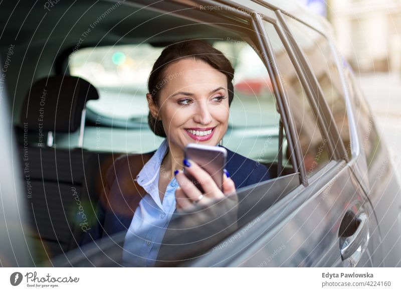 Junge Frau mit Smartphone auf dem Rücksitz eines Autos Carsharing selbstbewusst Lächeln Befriedigung attraktiv schön junger Erwachsener Freude positiv Inhalt