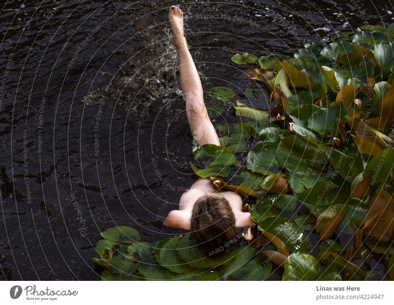 Dieses dunkle Wasser hält nackte Mädchen nicht davon ab, darin zu schwimmen. Ein perfektes blondes Model mit einem perfekten Körper hat Spaß an einem heißen Sommerabend. Seerosen, sexy Kurven und eine absolut entspannte Atmosphäre in diesem Bild.