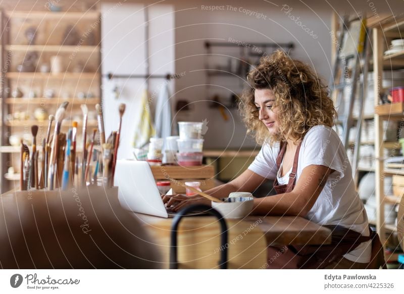 Frau Töpferin mit Laptop im Kunststudio Töpferwaren Künstler Keramik Arbeit arbeiten Menschen jung Erwachsener lässig attraktiv Glück Kaukasier genießend