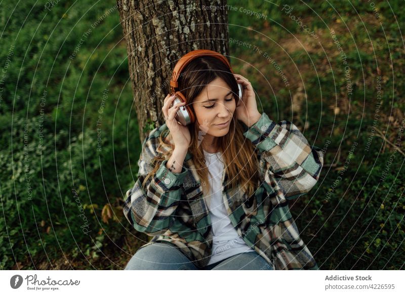 Lächelnde Frau genießt ein Lied über Kopfhörer in der Natur Musik meloman zuhören Gesang Melodie Landschaft benutzend Apparatur Gerät Inhalt Tattoo