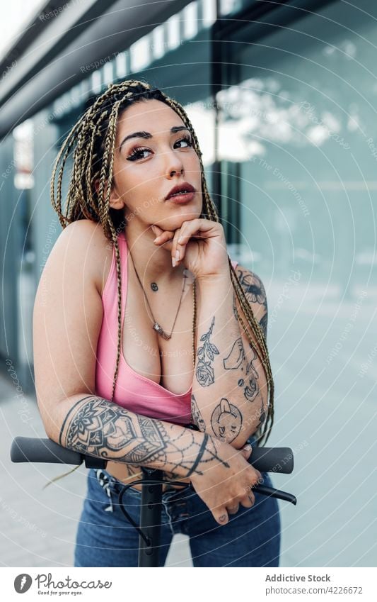 Tätowierte Frau auf Motorroller in der Stadt Individualität Tattoo cool Streetstyle Geflecht Tretroller tausendjährig Großstadt Porträt nachdenken