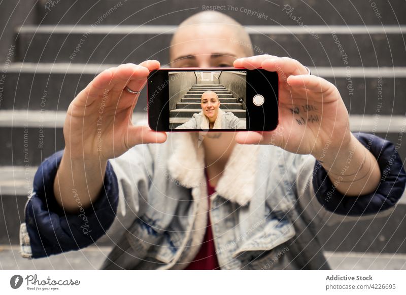 Lächelnde Queer, die ein Selfie mit ihrem Smartphone auf einer Treppe macht Transgender heiter Gedächtnis Moment Bildschirm Individualität Treppenhaus benutzend