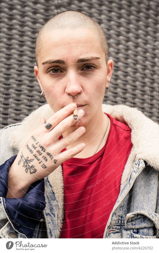 Transsexuelle Person mit Tattoo raucht Zigarette auf grauem Hintergrund Transgender Rauch selbstbewusst eitel Individualität cool Streetstyle Porträt queer