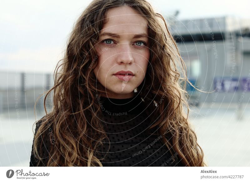 Portrait einer jungen Frau mit langem, brünettem, lockigem Haar auf dem obersten Parkdeck eines Parkhauses junge Frau 18-30 Jahre schön Schönheit Haare