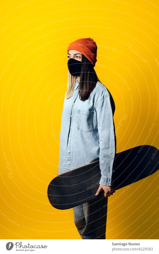 Mädchen mit Skateboard Portrait Atelier gelber Hintergrund Porträt Blick auf die Front Ausdruck farbenfroh Frisur lässig jung Frau ernst zwei Farben Haar