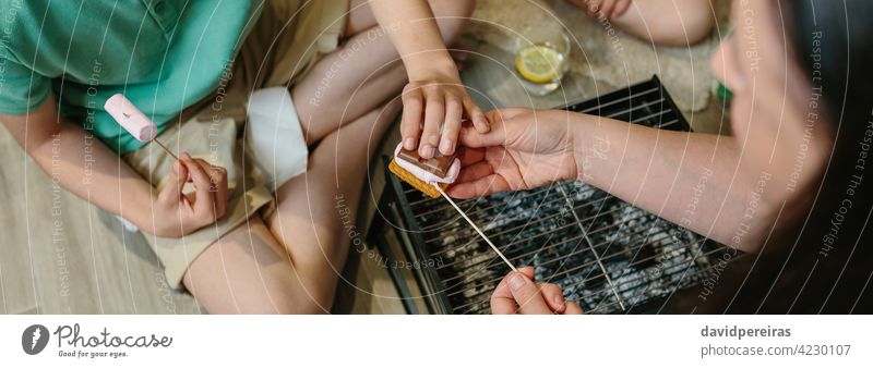 Draufsicht auf eine nicht zu erkennende Familie, die zu Hause Smores macht unkenntlich Herstellung S'mores Rauchwaren Marshmallow Schokolade Keks Röstung