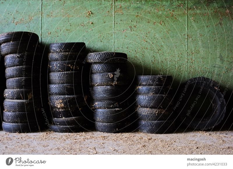 Mehrere Reifenstapel in einer Garage Stapel schwarz Grün Schatten niemand menschenleer Innenaufnahme Gummi alt Recycling Werkstatt Scheune Altreifen Müll