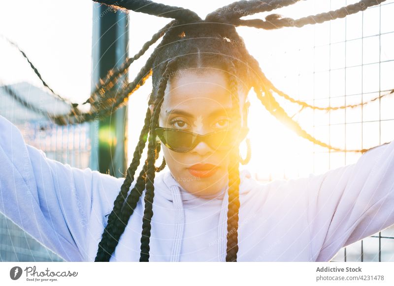 Coole schwarze Frau mit Afrozöpfen auf der Straße im Sonnenschein Afro-Look Geflecht Mode Sonnenbrille cool Streetstyle Individualität Porträt selbstbewusst