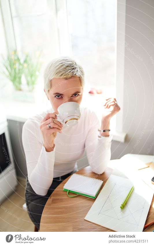 Astrologe trinkt Kaffee am Küchentisch im Haus trinken Heißgetränk Getränk feminin Tisch Frau Porträt heimwärts Tasse Astrologie Keramik Material Starrer Blick