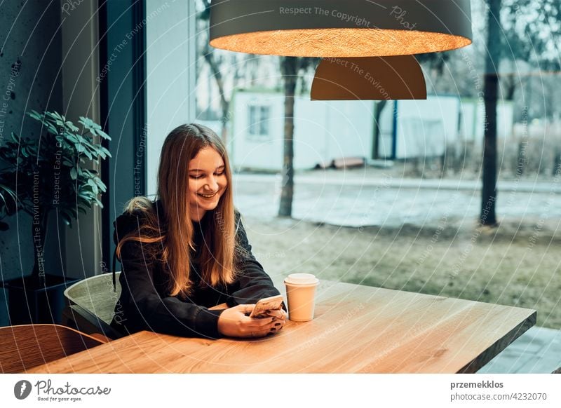 Junge Frau, die einen Videoanruf führt, aus der Ferne spricht, Kaffee trinkt und in einem Café sitzt. Mädchen entspannt sich im Café mit Mobiltelefon kaufen