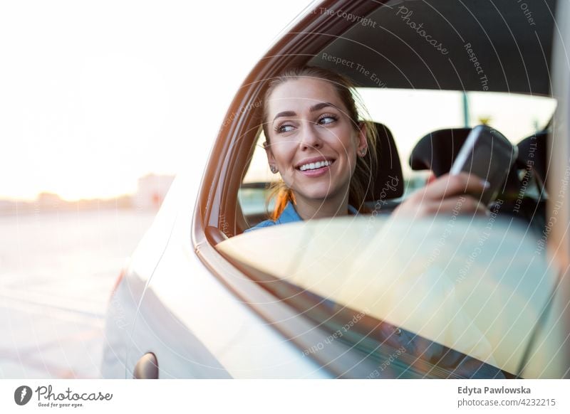 Junge Frau mit Smartphone auf dem Rücksitz eines Autos Carsharing selbstbewusst Lächeln Befriedigung attraktiv schön junger Erwachsener Freude positiv Inhalt