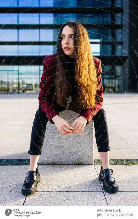 Stilvolle Frau sitzt gegen moderne Stadt Gebäude trendy urban Straße selbstbewusst emotionslos Vorschein Streetstyle Individualität ernst jung sitzen Outfit