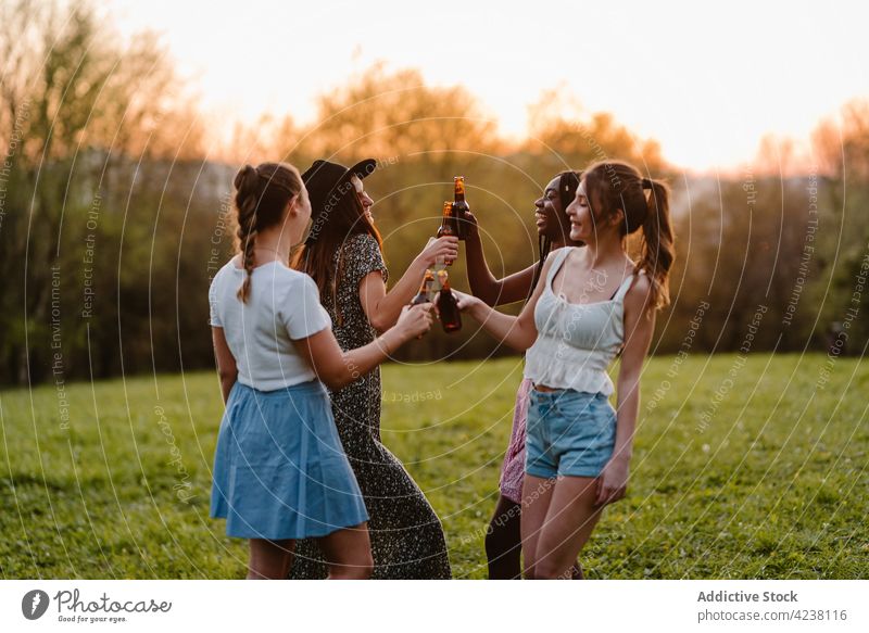 Gesellschaft von multirassischen Freundinnen, die bei Sonnenuntergang im Park auf Flaschen anstoßen Klirren Frauen Unternehmen Sommer Bier Kälte Spaß haben