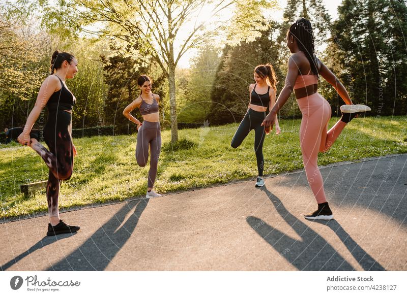 Multiethnische Sportlerinnen wärmen sich auf dem Gehweg im Stadtpark auf Aufwärmen Dehnung Training Bein angehoben Übung Park Großstadt Frauen