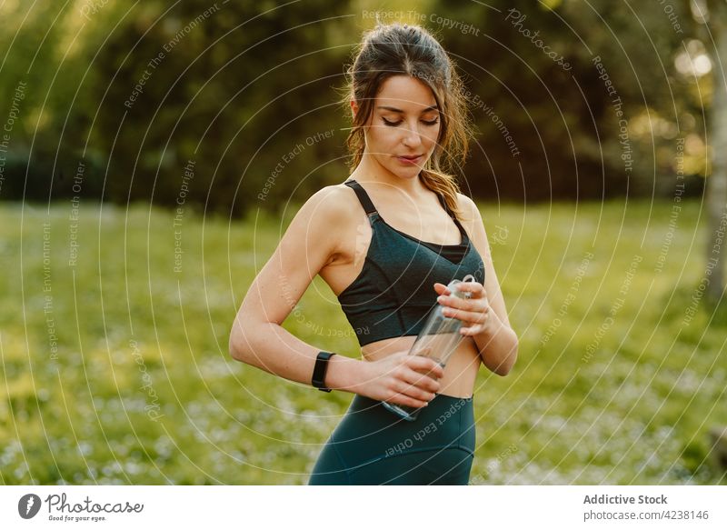 Sportler trinkt Wasser bei Sonnenschein Athlet Flasche trinken intelligente Uhr Herzschlag prüfen Pause Frau benutzend Gerät Wiese Sportlerin bewerten Training