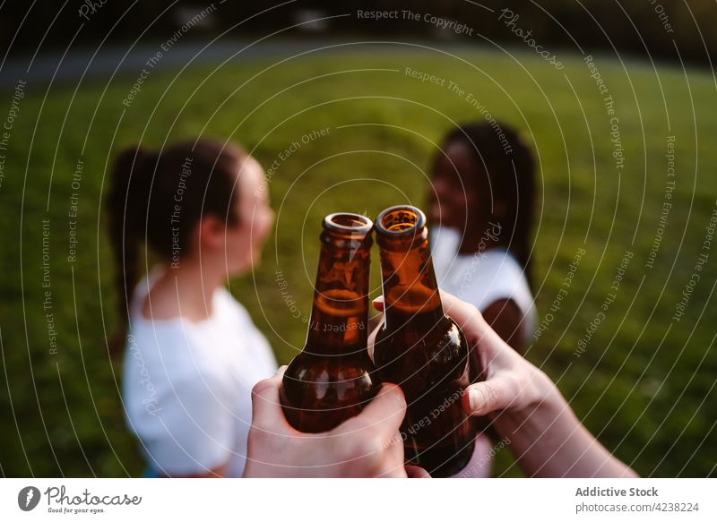 Gesellschaft von multirassischen Freundinnen, die bei Sonnenuntergang im Park auf Flaschen anstoßen Klirren Frauen Unternehmen Sommer Bier Kälte Spaß haben