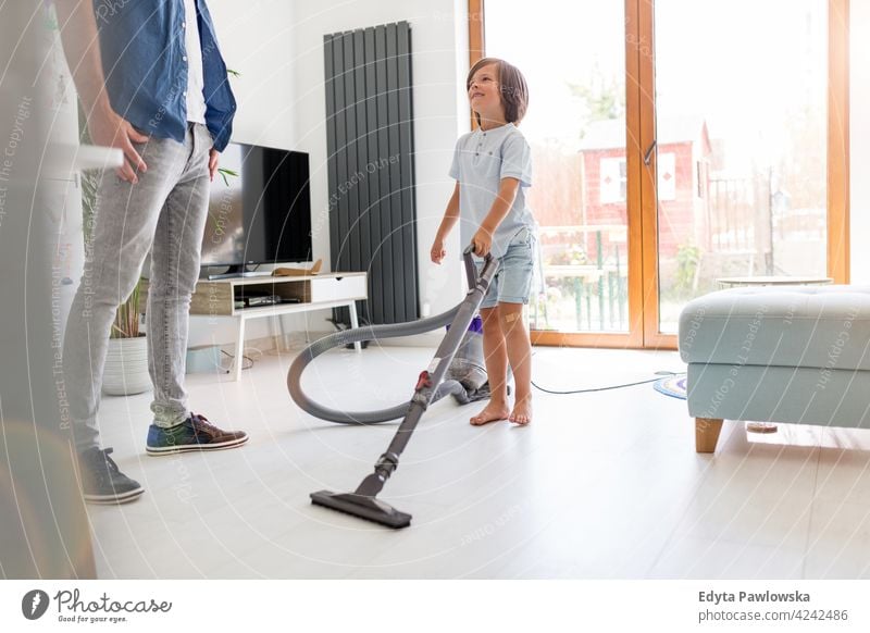 Junge staubsaugt Boden, während Vater zu Hause steht Staubsauger Stock Stehen Hilfe Hausarbeiten Staubsaugen Hausaufgabe Lernen im Innenbereich heimwärts Mann