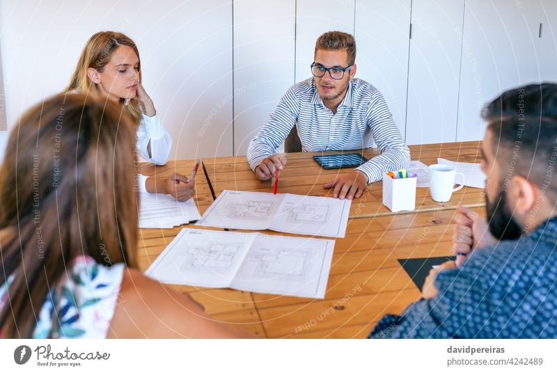 Geschäftsleute in einer Arbeitsbesprechung beim Betrachten von Konstruktionszeichnungen Architekt Arbeitstreffen Teamwork Büro Holztisch Hauspläne sprechend