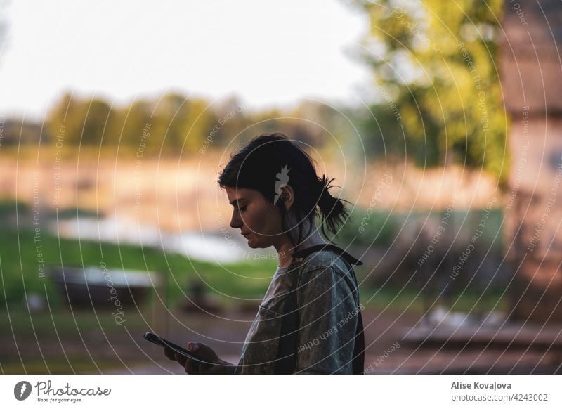 Wie lange können Sie ohne Ihr Telefon auskommen? Mädchen am Telefon Porträt Telefon in der Hand außerhalb dunkles Haar Blick auf das Telefon Lifestyle Frau