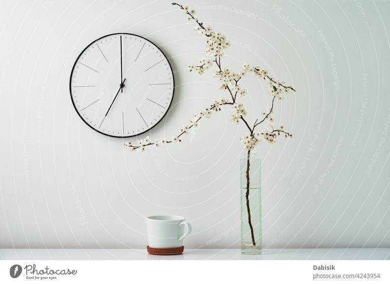 Wanduhr, blühender Zweig und Tasse auf weißem Hintergrund Uhr Dekor Blume sehr wenige Schreibtisch Raum Desktop heimwärts Attrappe stylisch Zeit dekorieren Ast