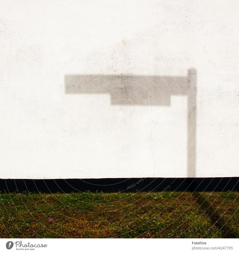 Der Schatten eines Straßenschildes fällt auf eine weiße Wand. grau schwarz grün Rasen Wiese Gras Mauer Abgrenzung Beton Betonwand Betonmauer gestrichen