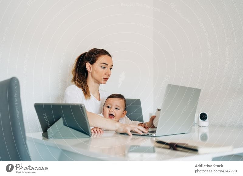 Mutter mit Laptop und Baby schaut Cartoons auf dem Tablet Zusammensein Schreibtisch Arbeit Browsen Glück Kinderbetreuung zu Hause Säuglingsalter Frau