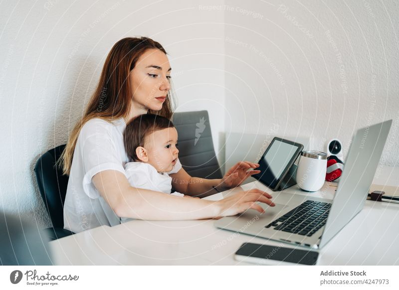 Mutter mit Laptop und Baby schaut Cartoons auf dem Tablet Zusammensein Schreibtisch Arbeit Browsen Glück Kinderbetreuung zu Hause Säuglingsalter Frau