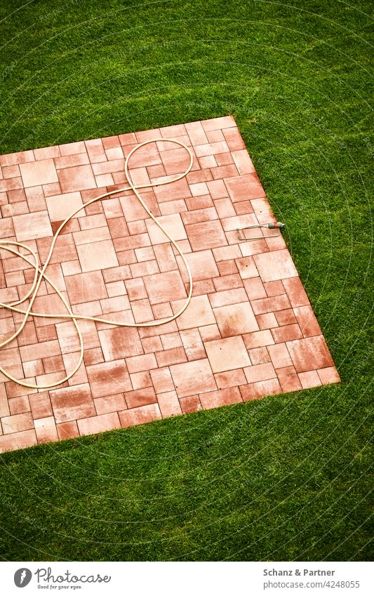 Terrassenplatten im Garten Gartenschlauch wässern Gartenarbeit Erholung Einfamilienhaus Platten Gras Wiese Rasen mähen Rollrasen Muster grün Sommer Gärtner