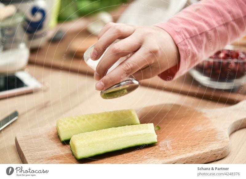 Kind würzt Gurkenstücke mit einem Saltstreuer Essen Nahrung gesundes essen grün Salz Hand kochen Salzstreuer Lebendmittel Ernährung Lebensmittel Gemüse Farbfoto