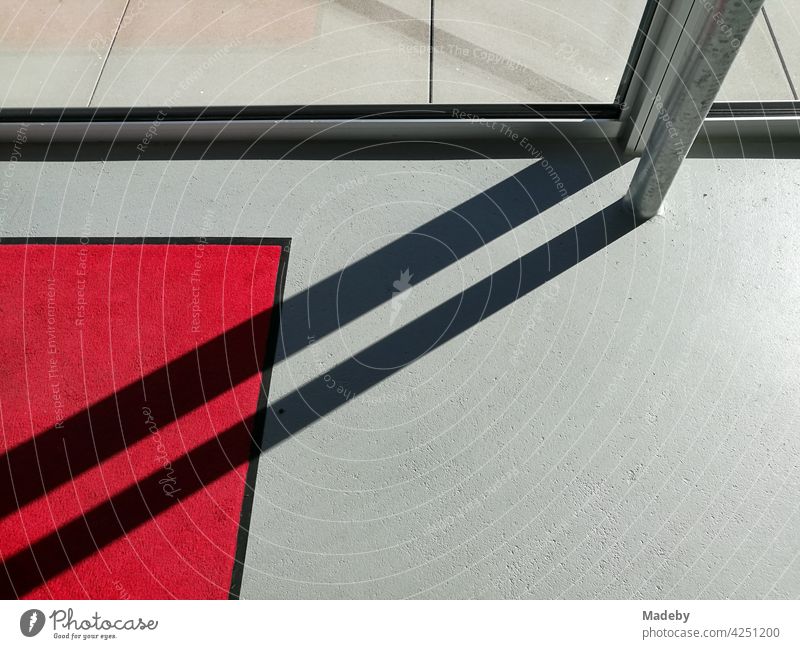 Diagonaler Schatten auf grauem Boden und rotem Teppich im Eingangsbereich einer Galerie in moderner Architektur in Oelde in Westfalen Licht Sonnenschein Grau