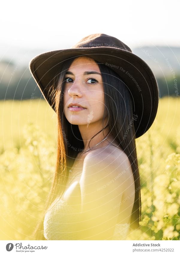 Gelassene Frau auf blühendem Feld stehend gelb Blume sensibel Blüte filigran feminin nackte Schultern Natur Blütezeit Gelassenheit friedlich Hut attraktiv schön