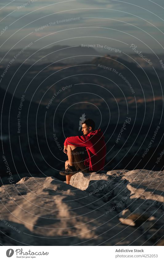 Unbekannter Mann auf rauem Berggipfel ruhend Wanderer Berge u. Gebirge Hochland Sonnenuntergang bewundern Natur Reisender Trekking sitzen nachdenklich Felsen