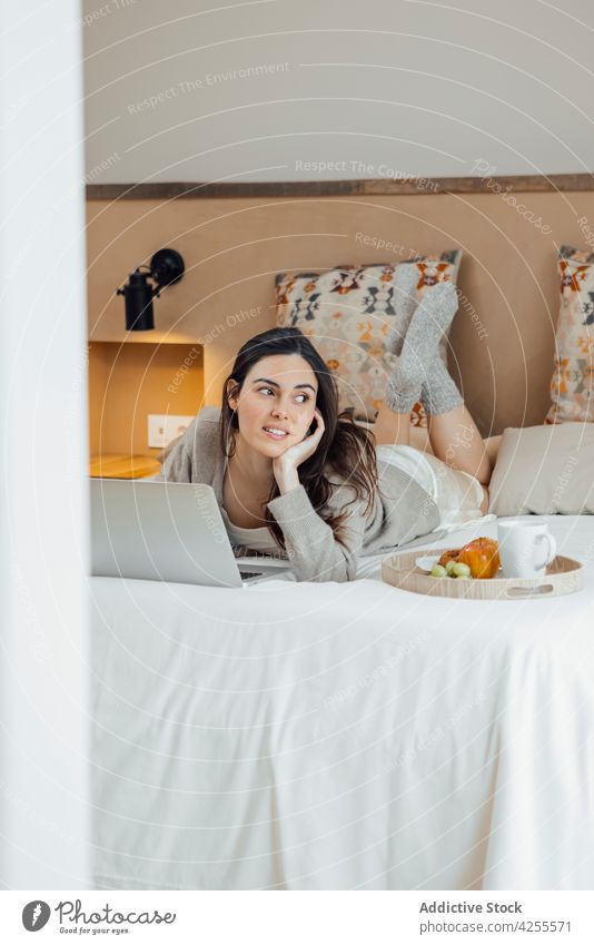 Positive Frau mit Laptop auf dem Bett Inhalt benutzend Morgen Frühstück Schlafzimmer Browsen Lügen heimisch Gerät Internet online Apparatur Lächeln Netbook