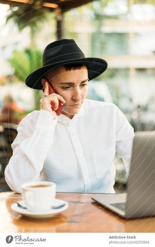 Ernsthafter Junge, der mit seinem Handy telefoniert, während er am Laptop arbeitet Frau Wildfang benutzend Smartphone Telefonanruf digital freiberuflich Arbeit