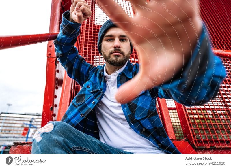 Mann mit blauem Hut und kariertem Hemd in der Nähe einer Metallkonstruktion kariertes Hemd Konstruktion bügeln selbstbewusst Faust zeigen gestikulieren cool