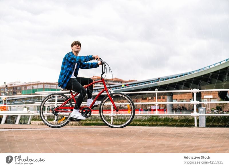 Mann in blau kariertem Hemd fährt auf einem städtischen Platz Fahrrad Mitfahrgelegenheit kariertes Hemd lässig Reling Aktivität heiter urban Glück männlich