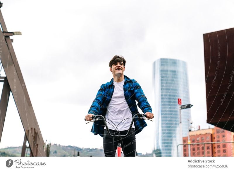 Mann in blau kariertem Hemd fährt auf einem städtischen Platz Fahrrad Mitfahrgelegenheit kariertes Hemd lässig Reling Aktivität heiter urban Glück männlich