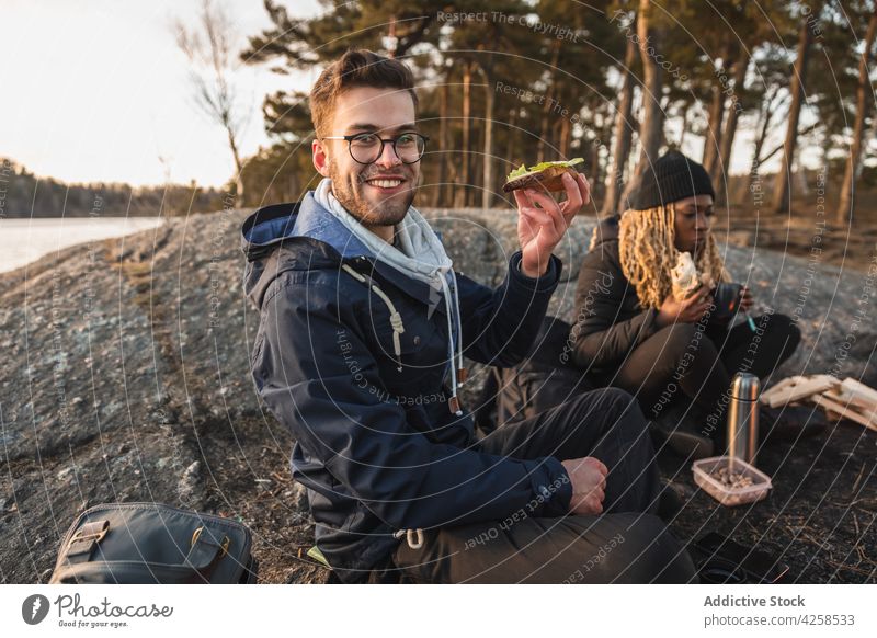 Happy diverse Freunde mit Picknick in der Nähe von See umgeben von Wald auf Herbst Tag Mann Frau Lager Reisender Lächeln Zusammensein Belegtes Brot hungrig