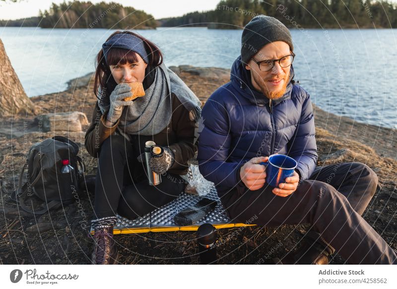 Freunde trinken Tee und essen am Flussufer Frau Mann positiv Lebensmittel Picknick Reise Ufer männlich See Natur Zusammensein sitzen jung Lächeln Getränk