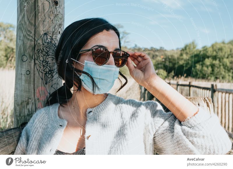 Frau mit Sonnenbrille und eine Gesichtsmaske lächelnd in die Kamera, während auf dem Land Hof während einer super sonnigen Tag mit Kopie Raum und Lifestyle Schuss